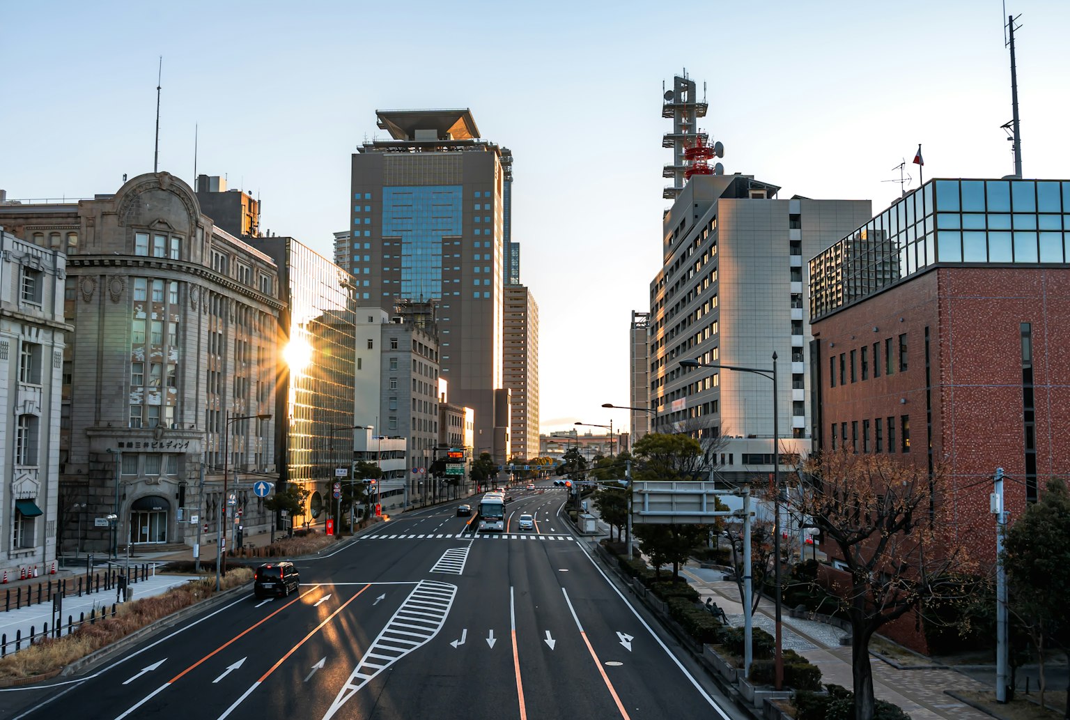 Urban landscape with sunset behind buildings, street traffic, quiet road, modern architecture