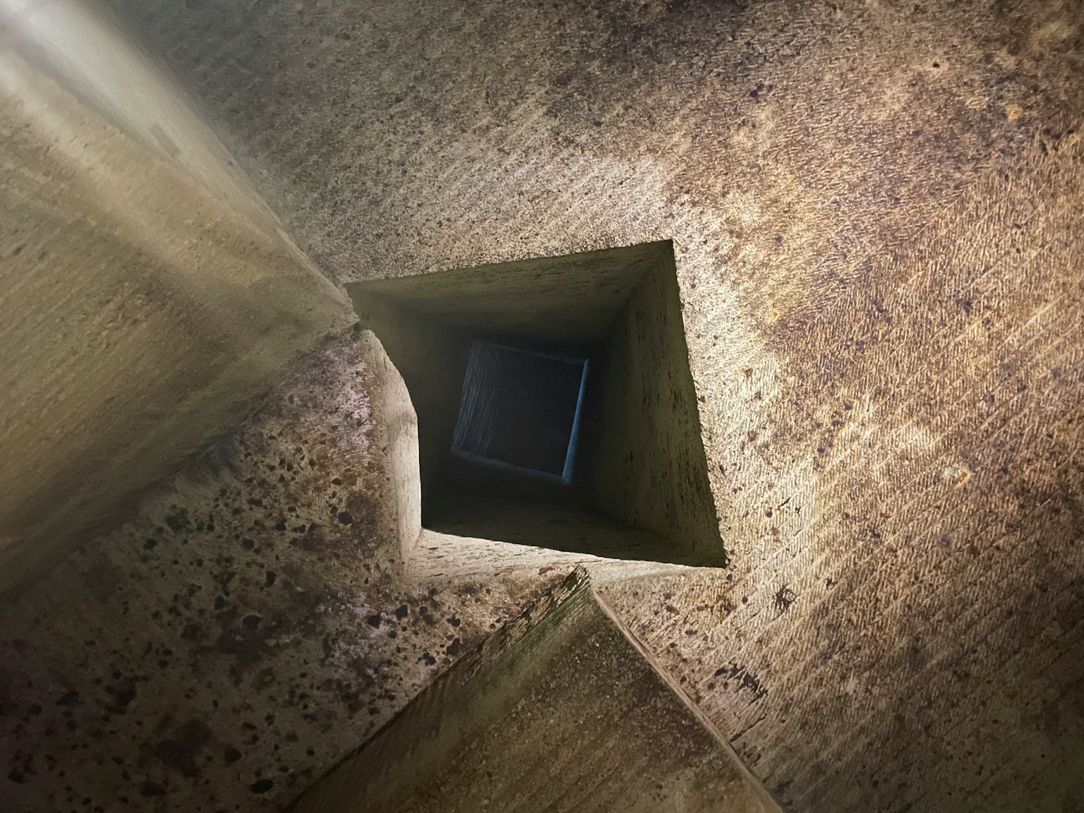 Vue vers le haut à travers un trou carré montrant des surfaces texturées et des effets de lumière