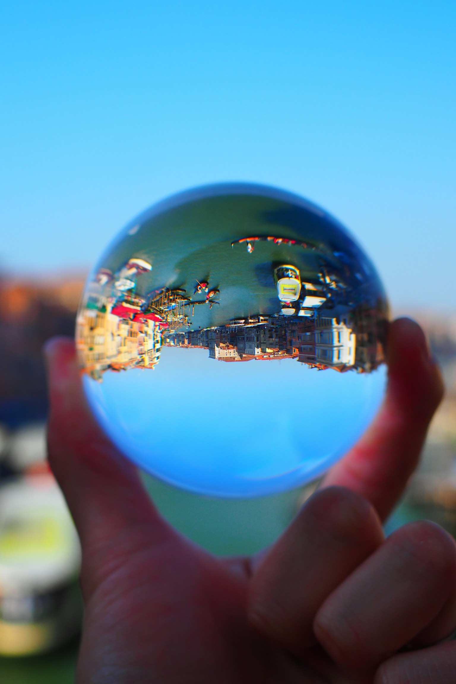 Una mano che tiene una sfera di cristallo trasparente che riflette un paesaggio bello contro un cielo blu