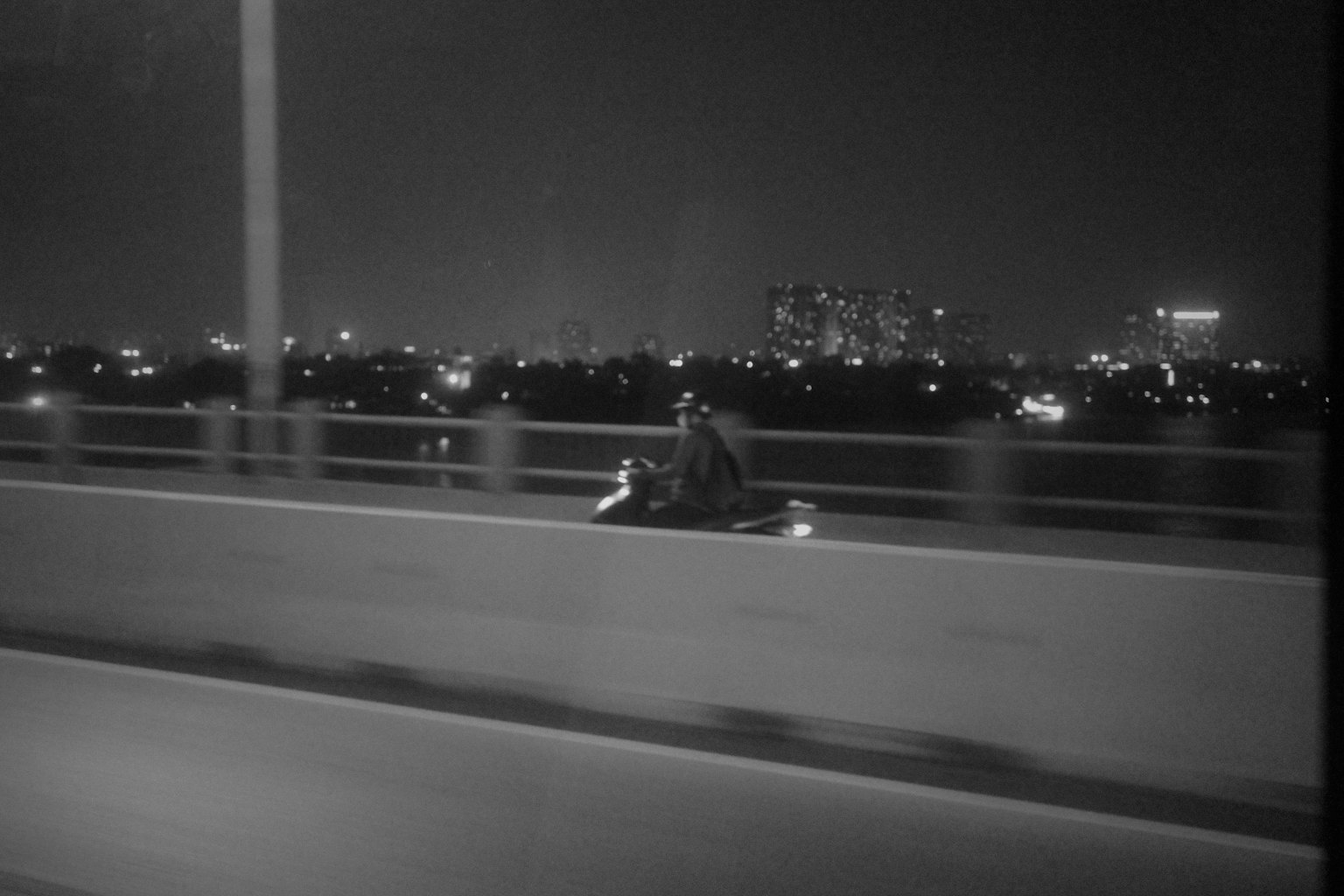 Motorcycle riding on a bridge at night with city lights in the background