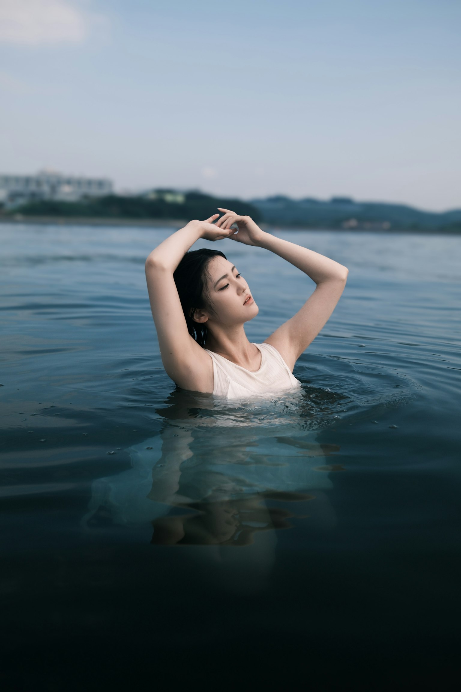 水に浸かる女性のポートレート、穏やかな表情、青い水面、背景に山々