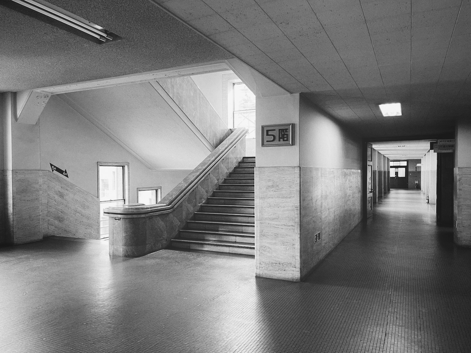 Interno di una scuola in bianco e nero con scale e un lungo corridoio