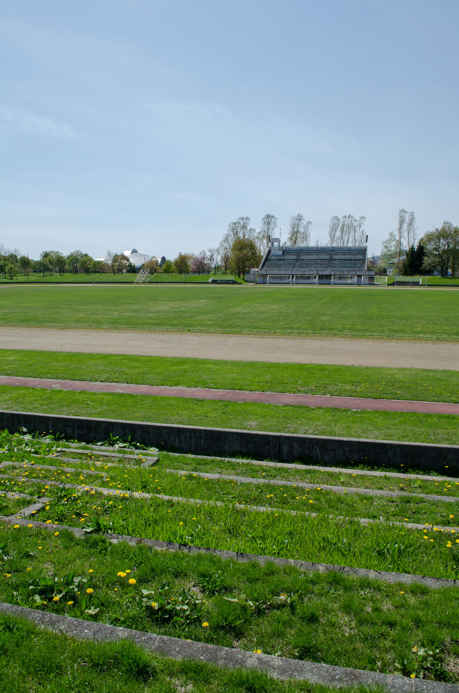 Lapangan rumput luas dengan tempat duduk penonton di fasilitas olahraga