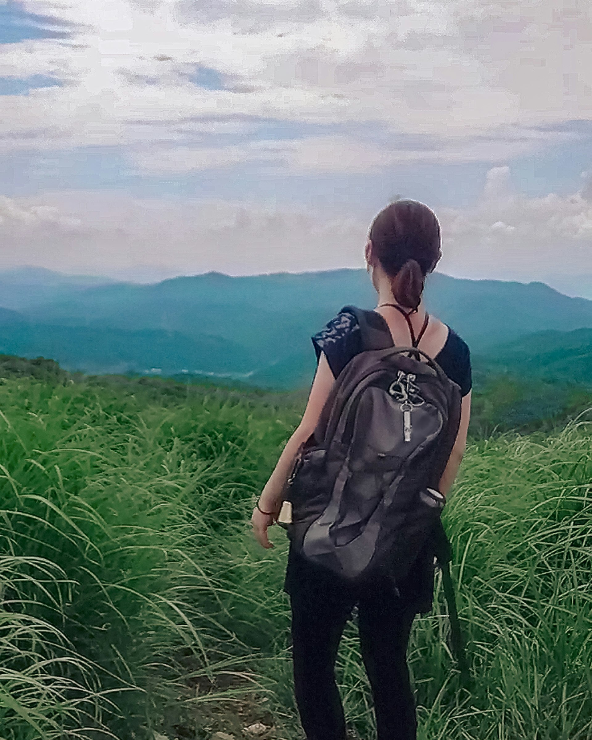 back view of a hiker with a backpack overlooking mountain ranges from a grassy hill