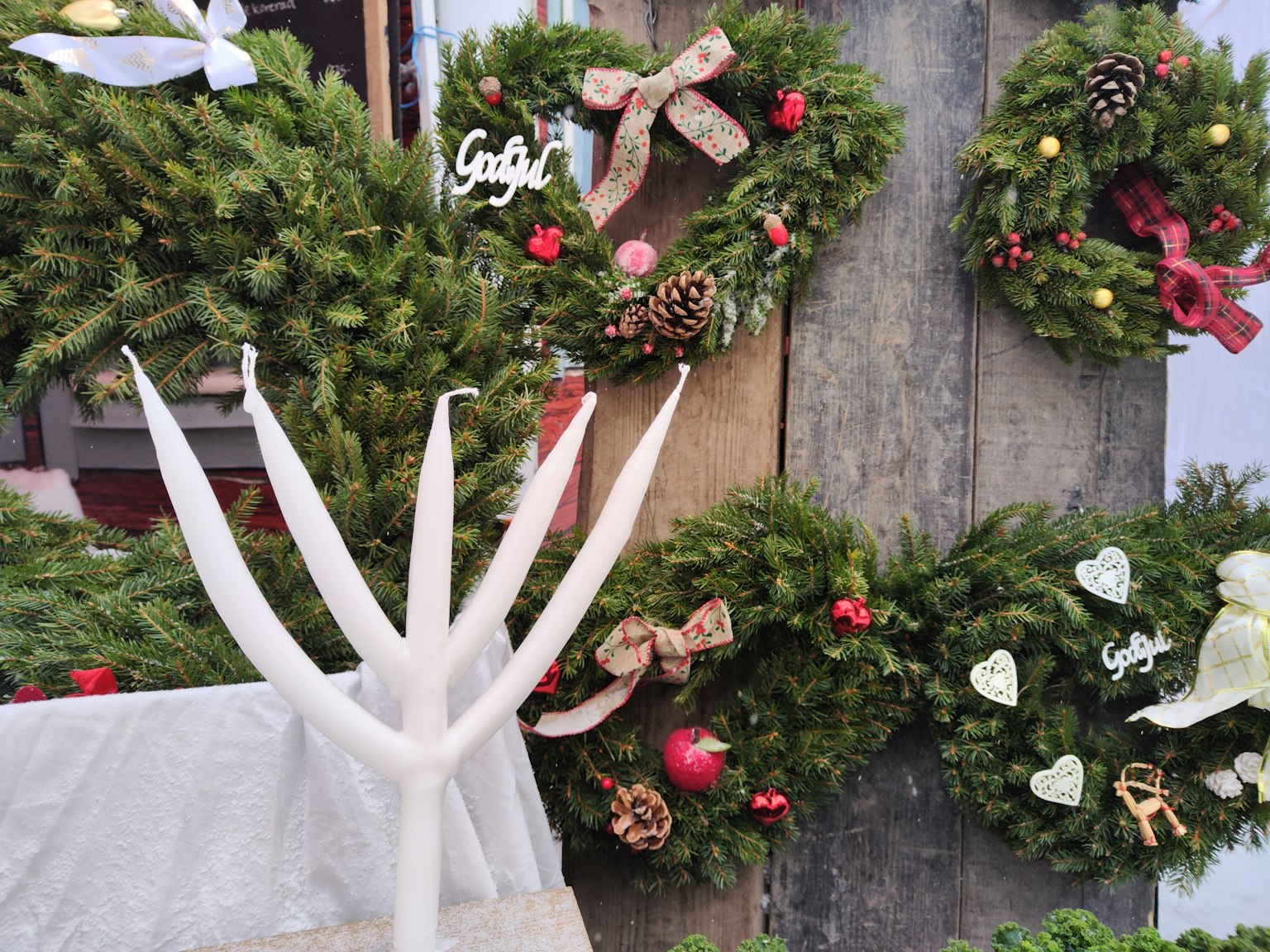 Coronas de Navidad decoradas con bayas rojas y lazos junto a un candelabro blanco
