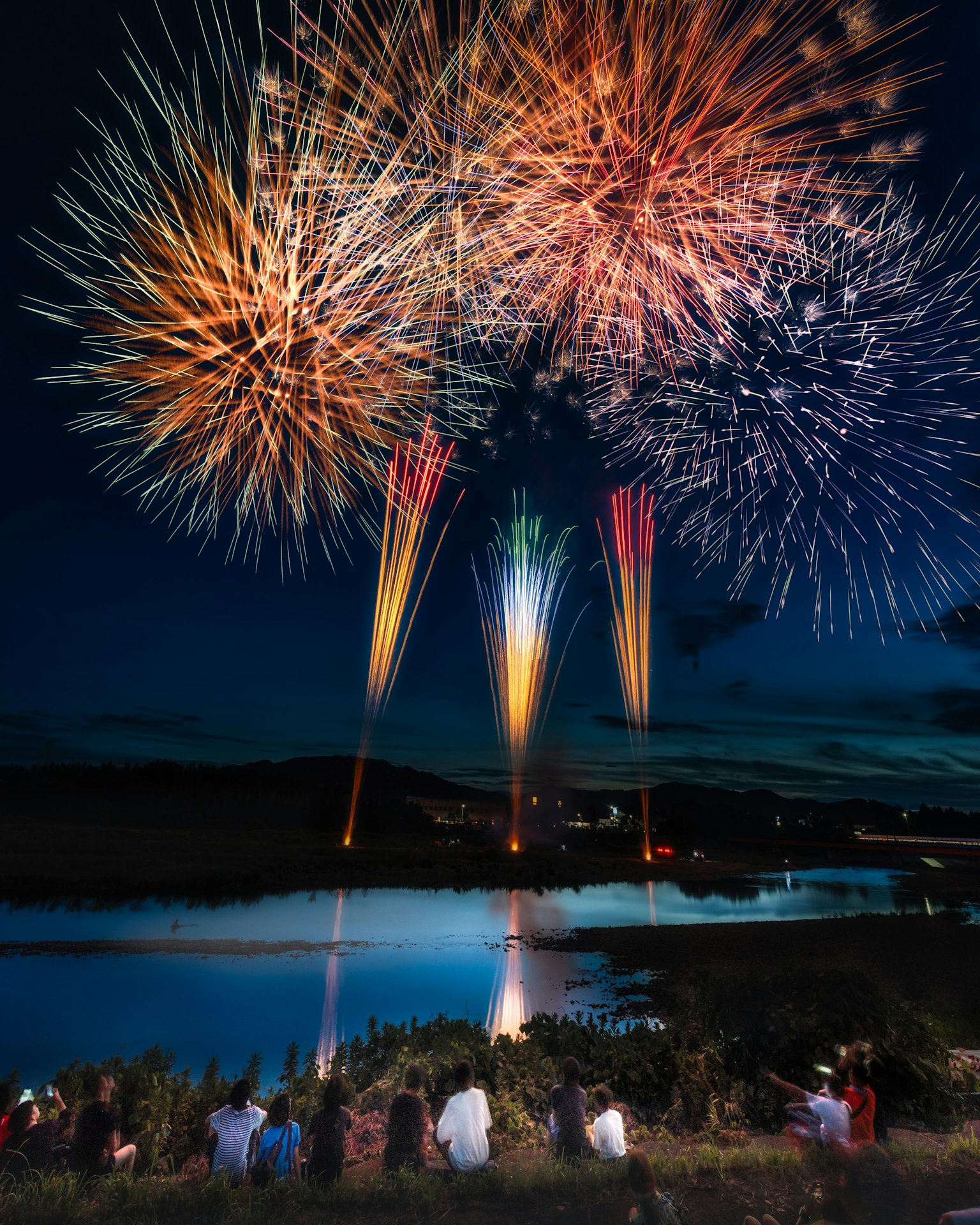 Un gruppo di persone che gode di fuochi d'artificio vivaci nel cielo notturno sopra un fiume