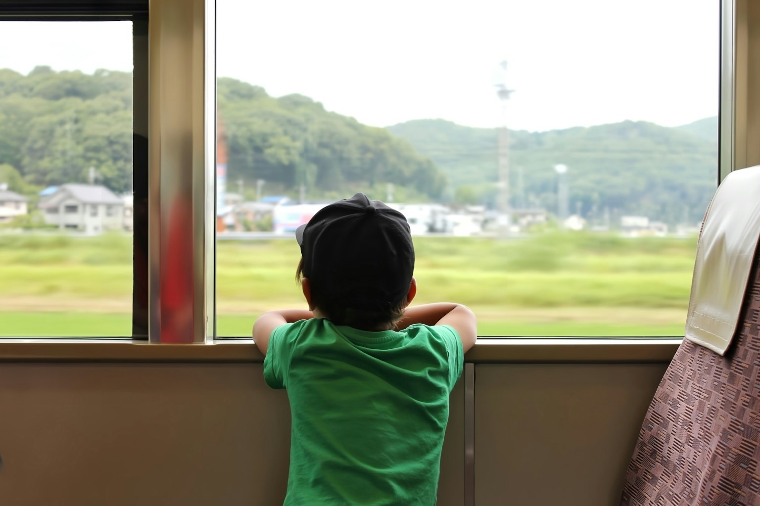 Un bambino con una maglietta verde che guarda fuori dal finestrino di un treno verso la campagna