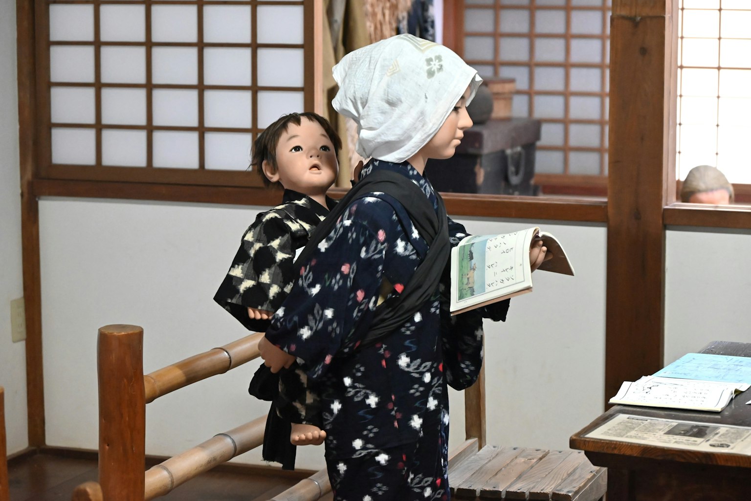 一個穿著和服、背著玩偶的男孩在傳統日本房間裡拿著一本書