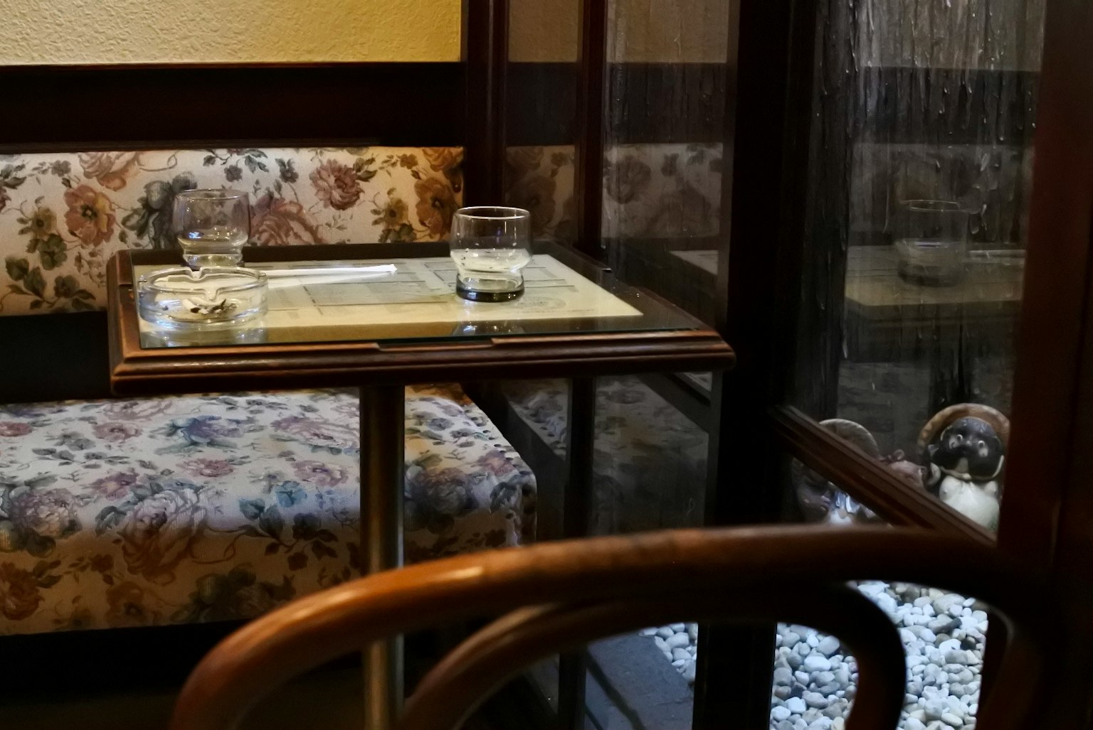 Gemütliches japanisches Café mit einem kleinen Tisch und Stuhl, Glas Wasser, blumiges Sofa, kleiner Garten draußen sichtbar