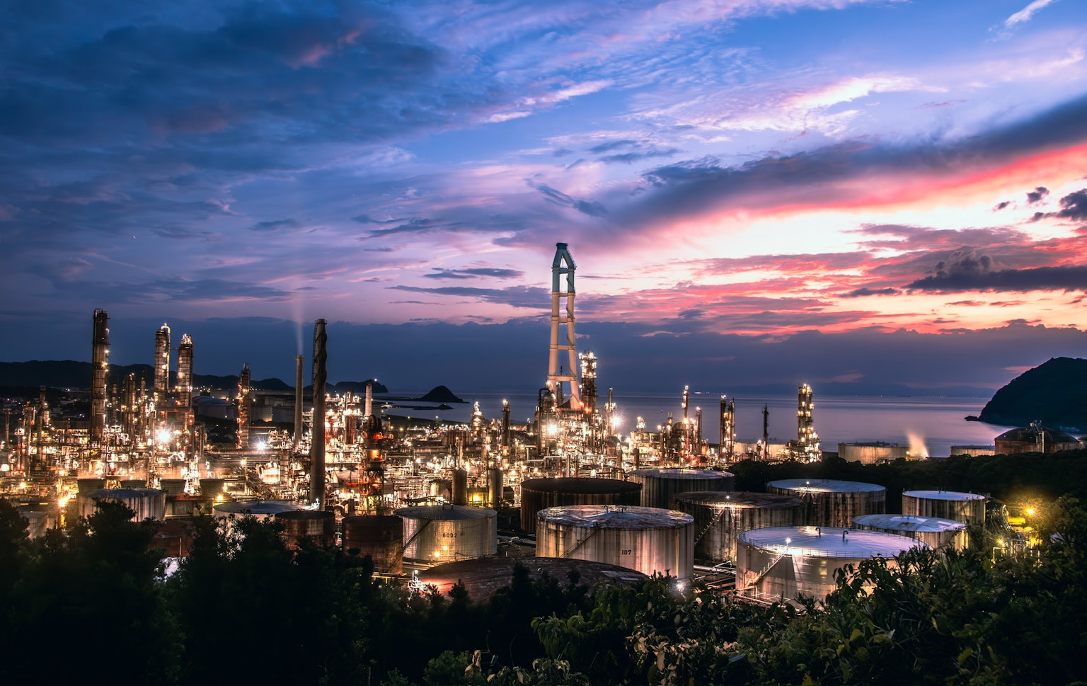 夕暮れ時の工業地帯の風景 明るい灯りが点在する石油精製所と海の景色