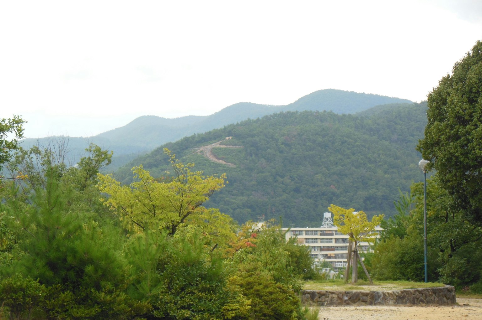 Vista panoramica di montagne verdi sotto un cielo nuvoloso con edifici bassi in primo piano