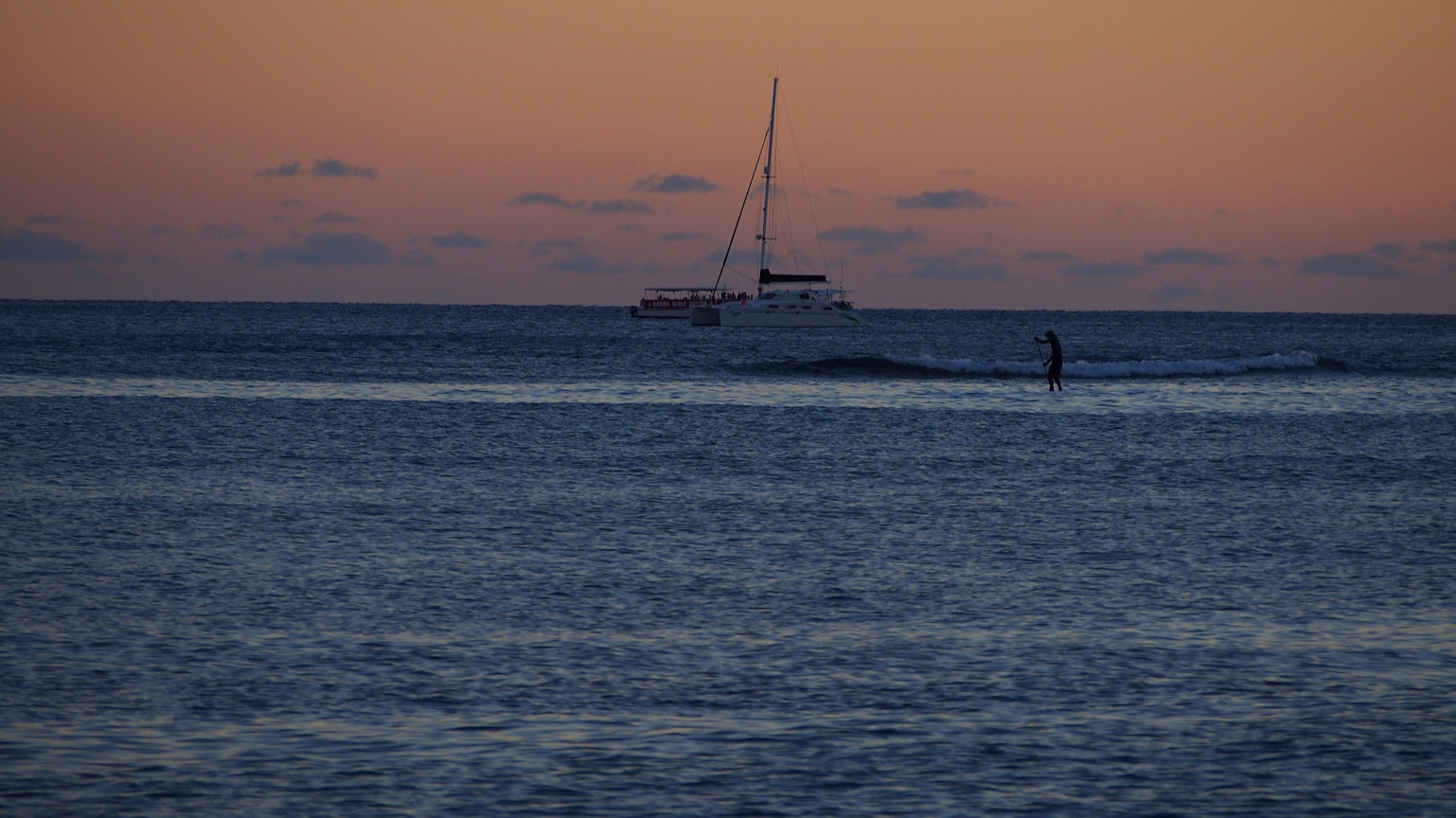Sailboat on the ocean at sunset with a person surfing