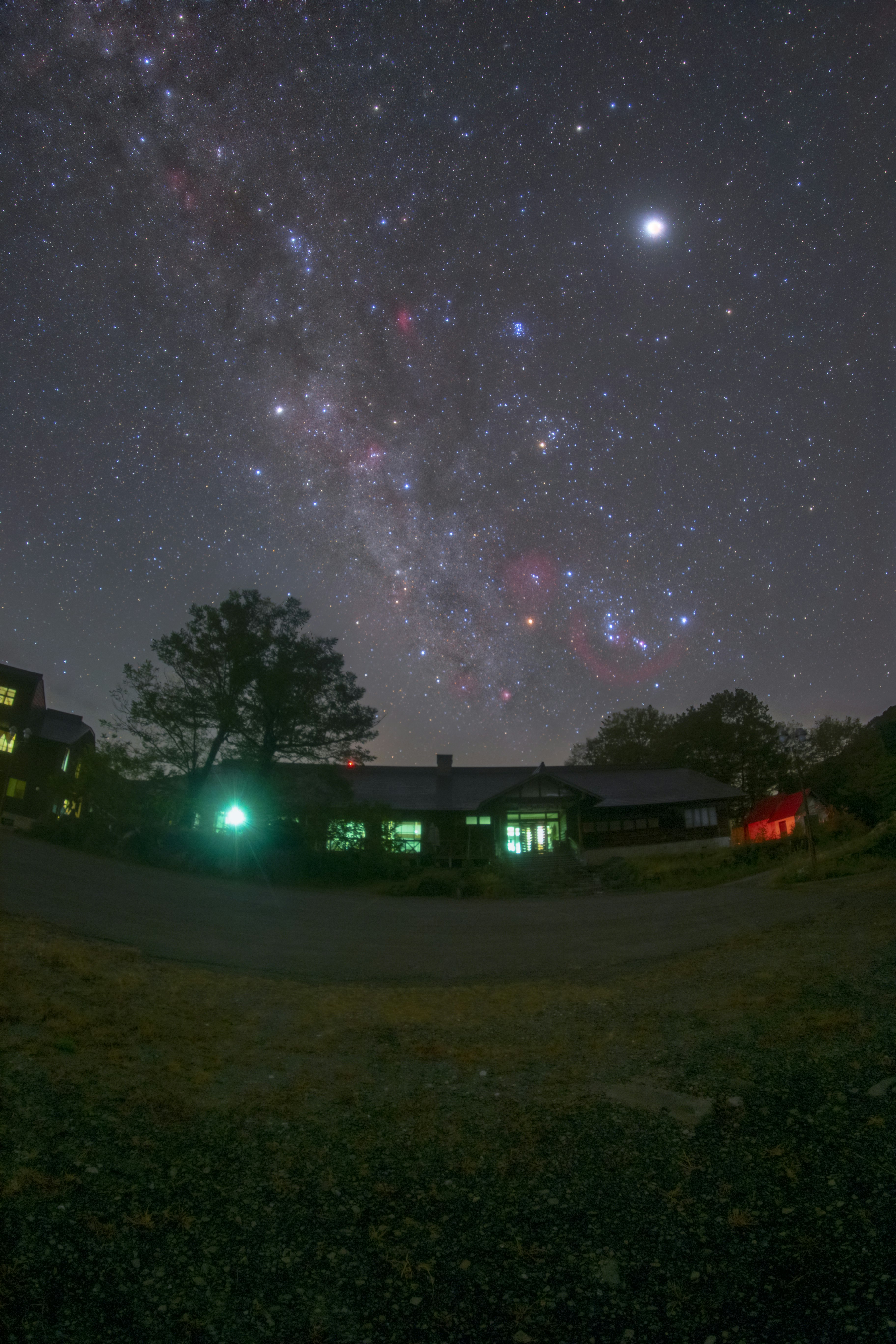 夜空に広がる天の川と星、草地の向こうの灯り