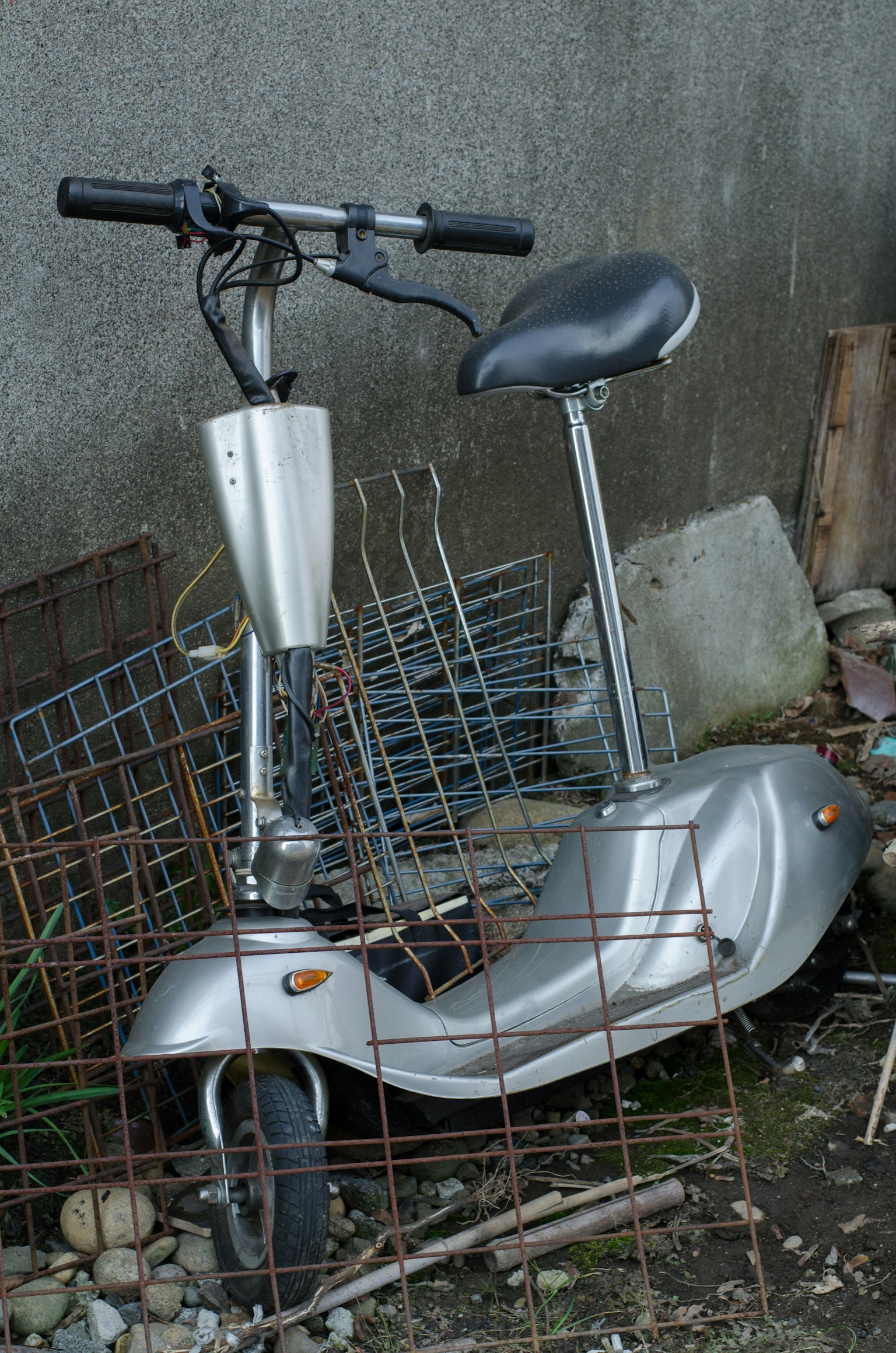 Un scooter eléctrico plateado oxidado colocado entre escombros