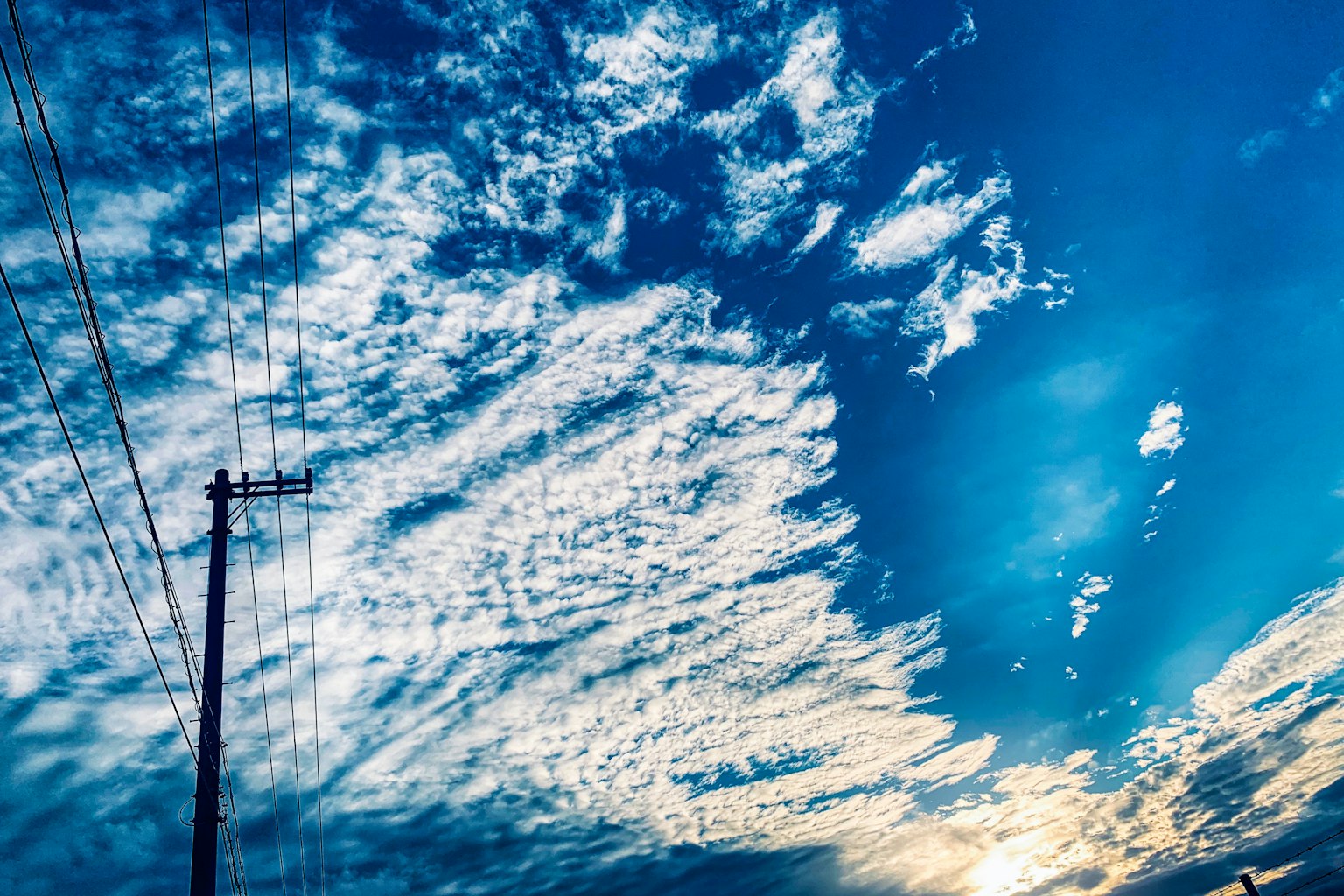 Silueta de un poste de electricidad contra un cielo azul lleno de nubes