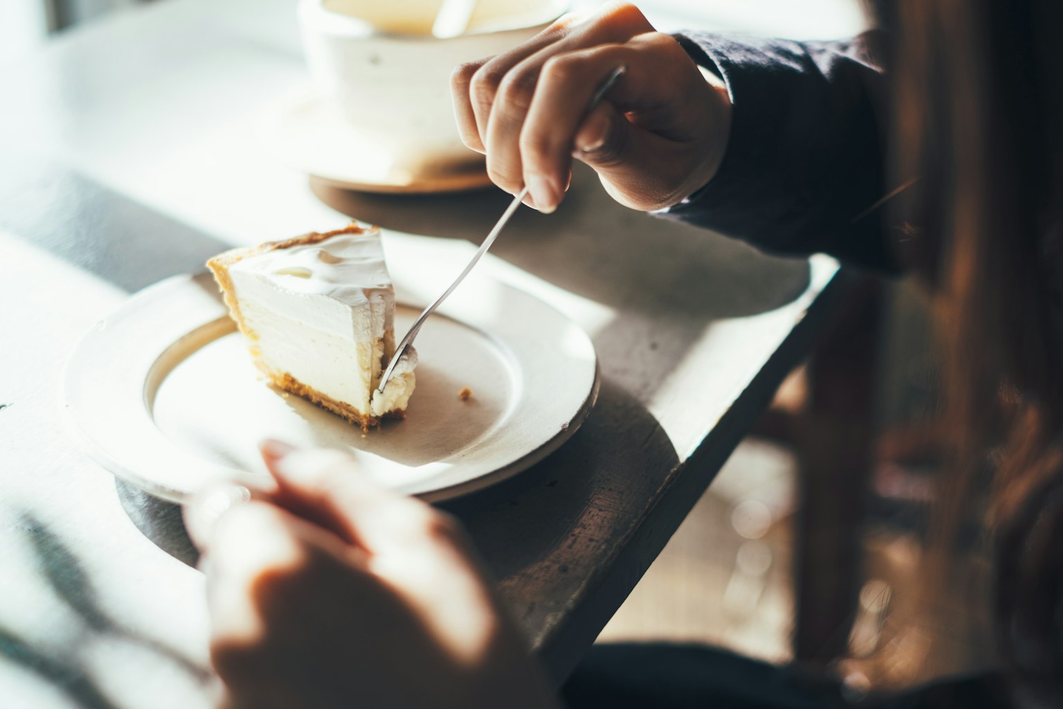 Primer plano de manos disfrutando de una porción de cheesecake en una mesa