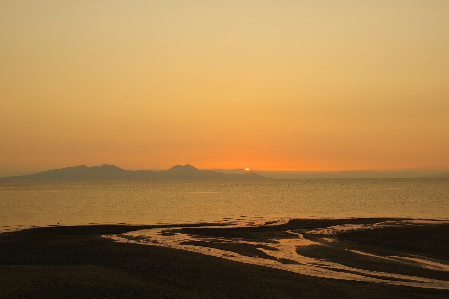 Tramonto sul mare con spiaggia di sabbia e corso d'acqua