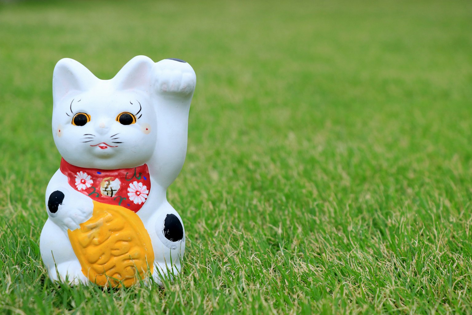 Una figura de gato de la suerte blanca sobre hierba verde