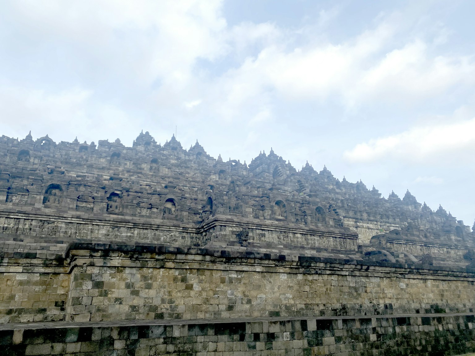 Vue latérale du temple de Borobudur montrant l'architecture en pierre ancienne sous un ciel nuageux