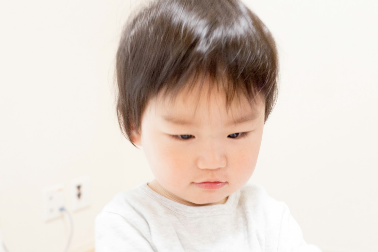 Un bambino con capelli neri corti che guarda verso il basso indossando una maglietta bianca
