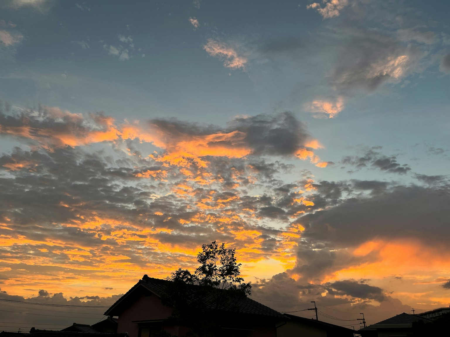 Un cielo de atardecer lleno de vibrantes tonos naranjas y azules sobre techos en silueta