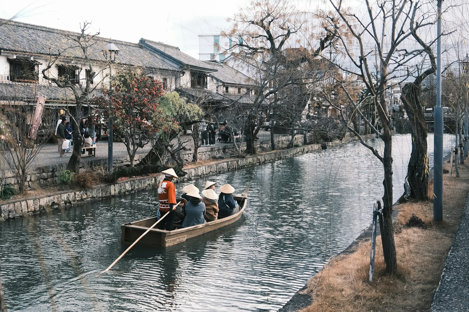 Un petit bateau avec des personnes pagayant le long d'un canal bordé de vieux bâtiments et d'arbres