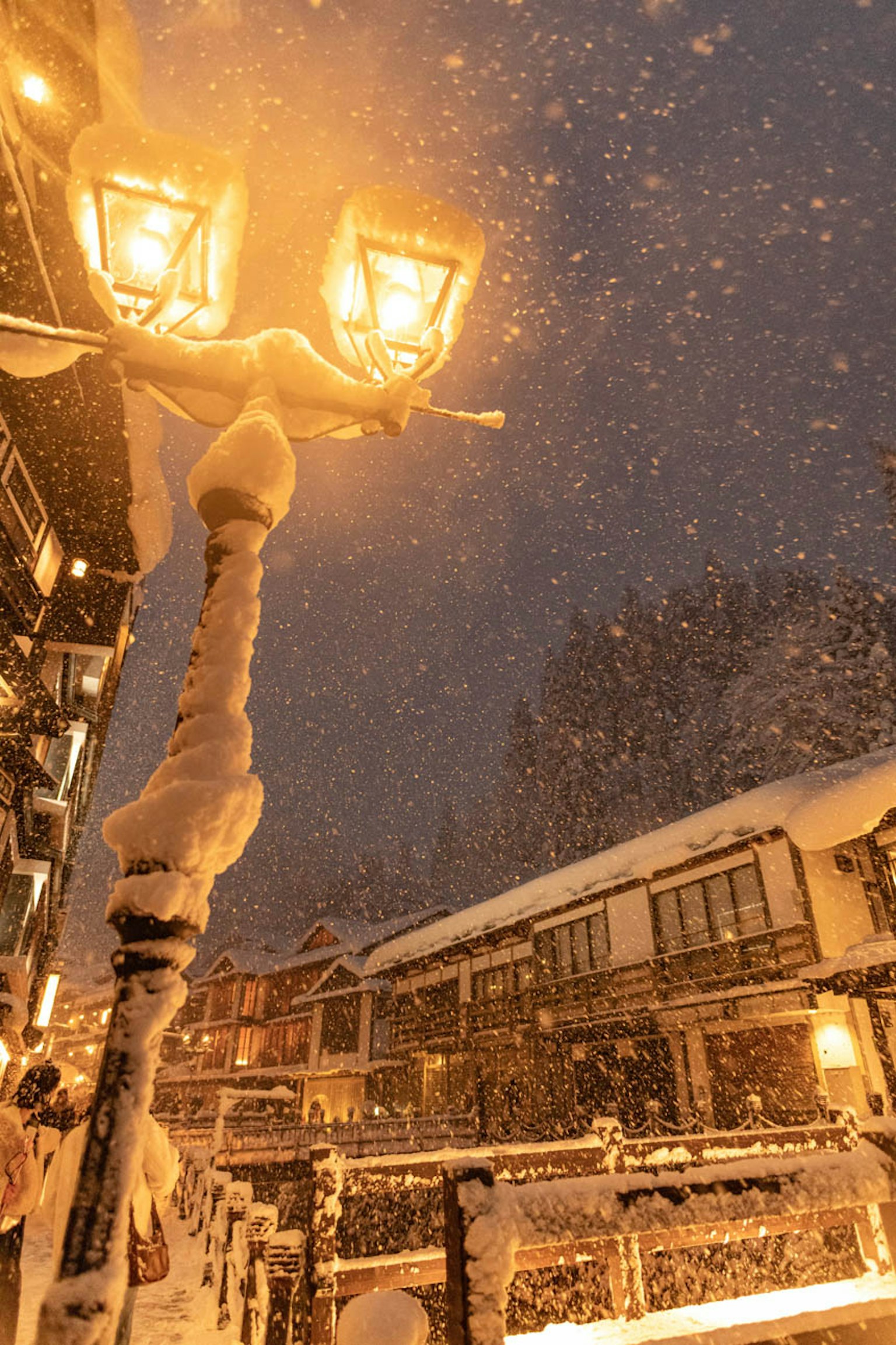 Une scène nocturne enneigée avec des lampadaires illuminés et des bâtiments recouverts de neige