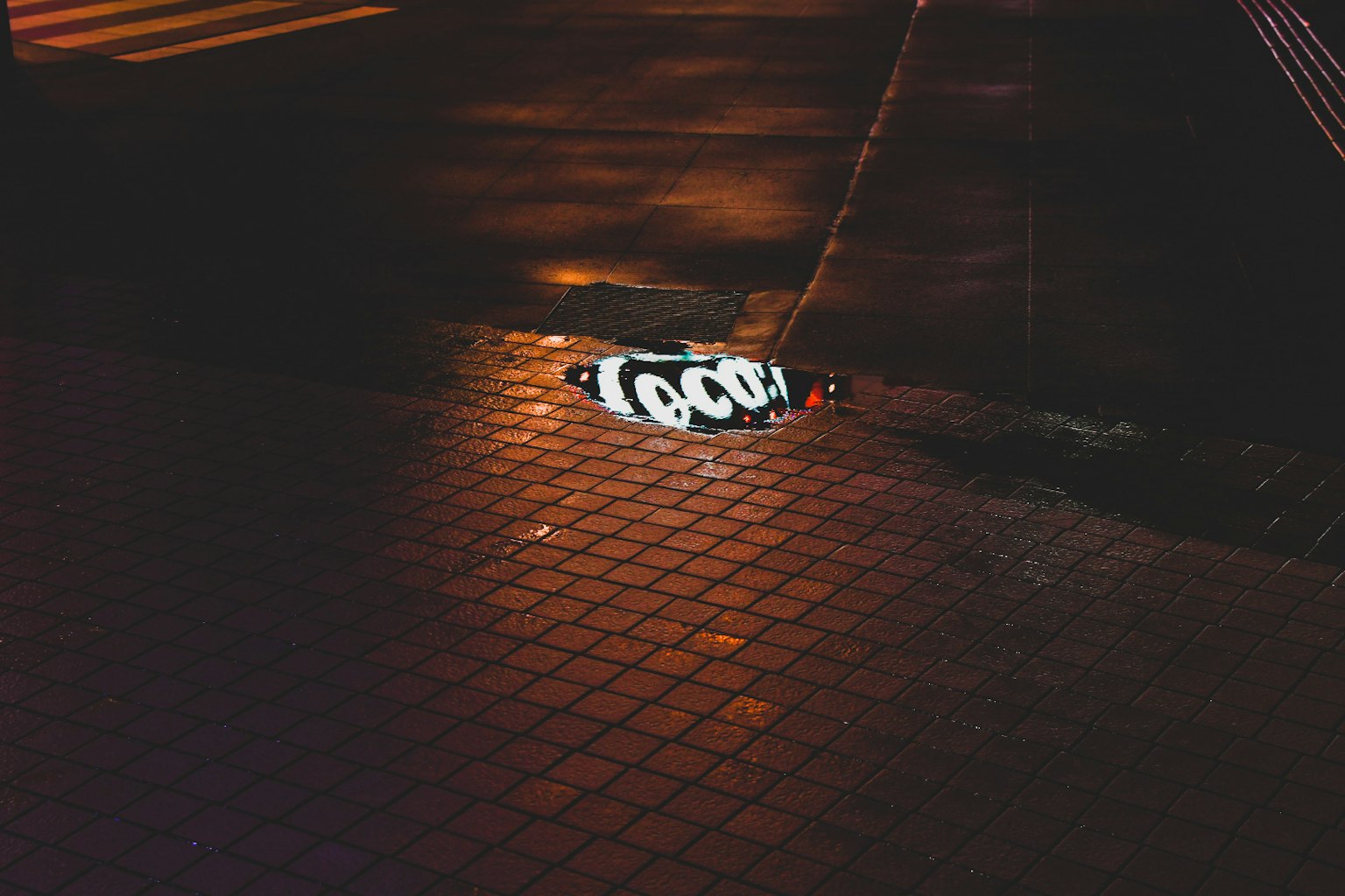 กราฟฟิตีที่อ่านว่า 'TOOL' สะท้อนอยู่ในรางน้ำมืดของถนน