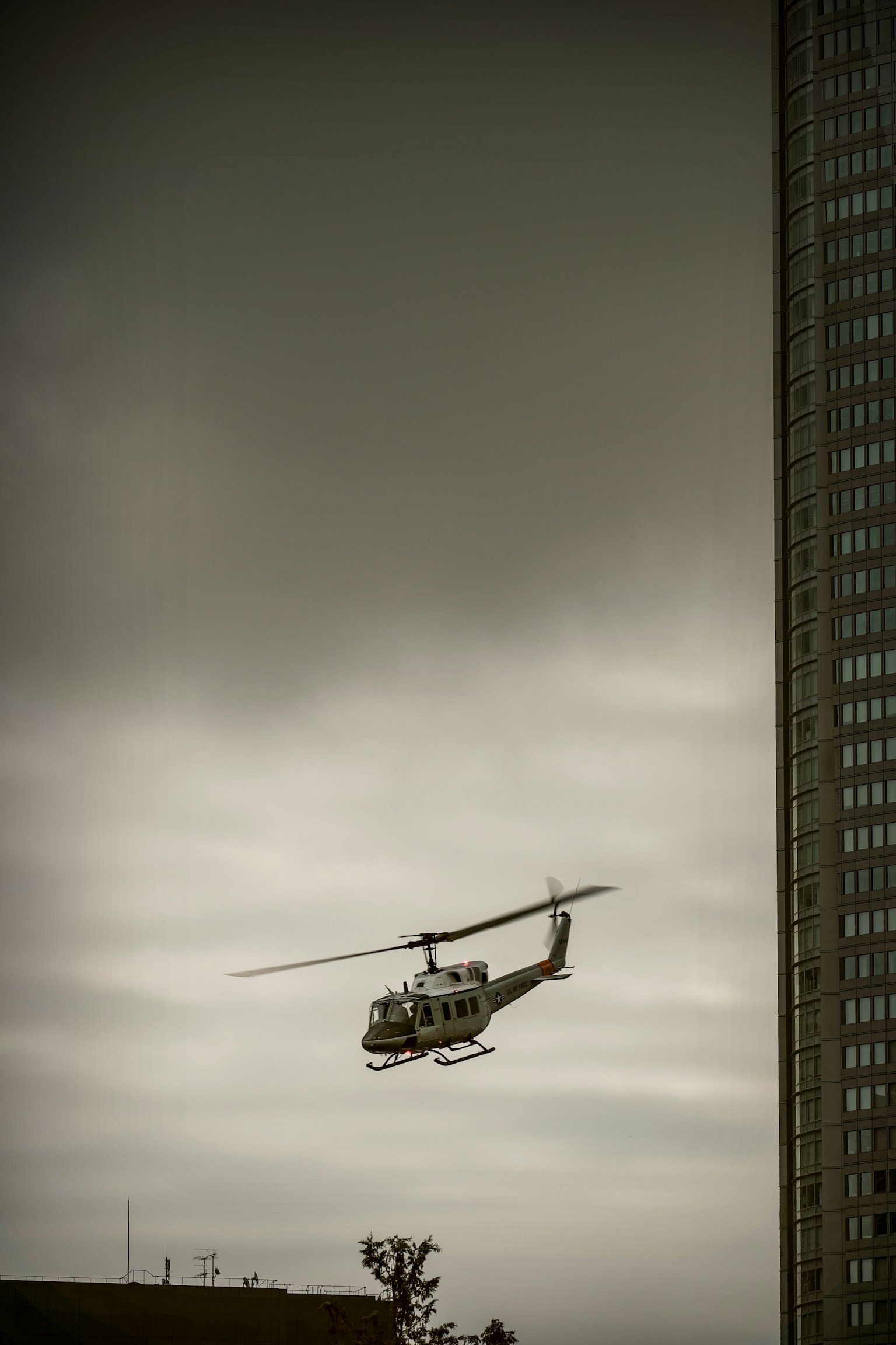Hubschrauber fliegt nahe einem Gebäude unter einem bewölkten Himmel