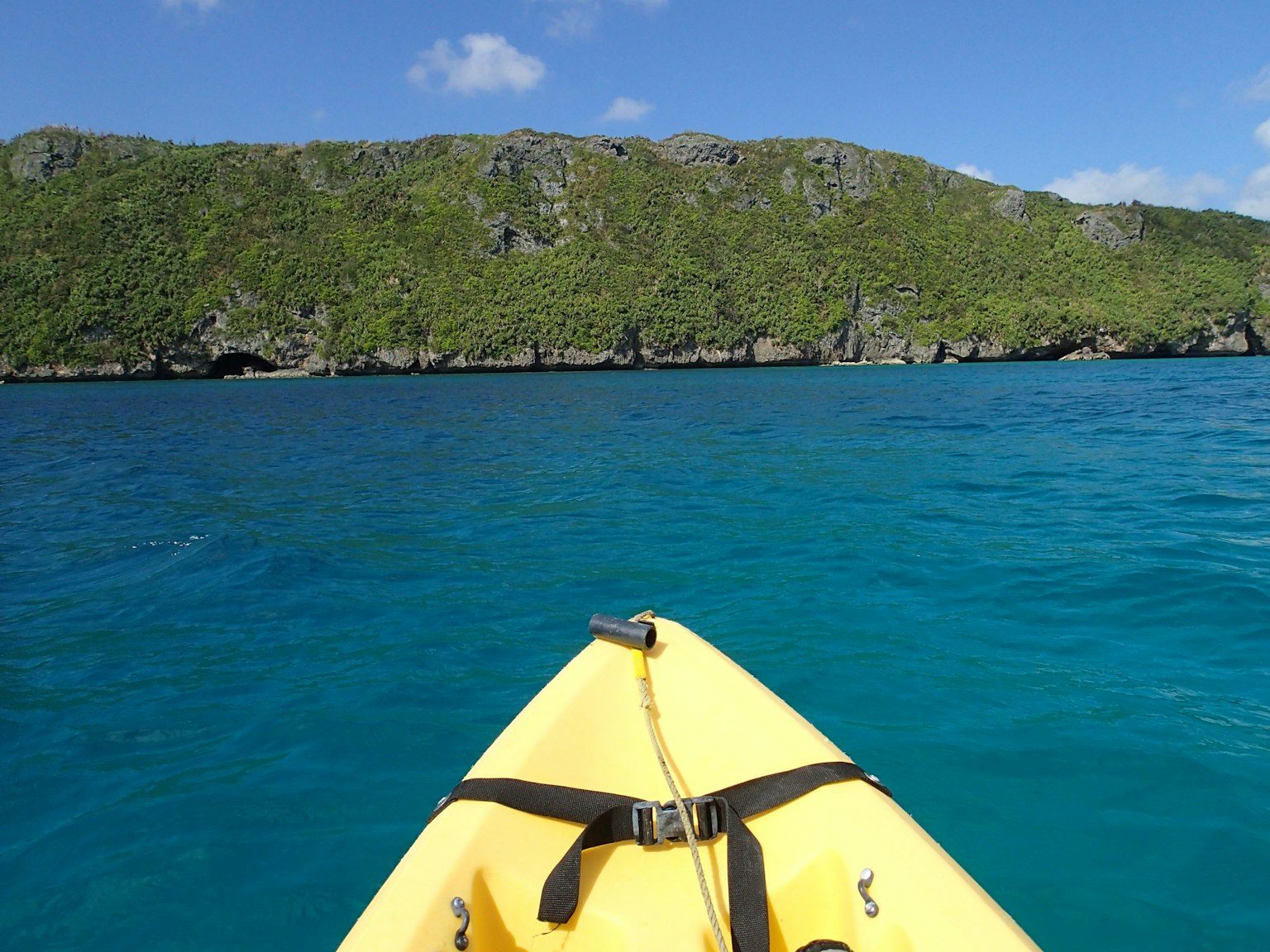 Un kayak jaune sur une eau bleue claire face à une côte rocheuse verte