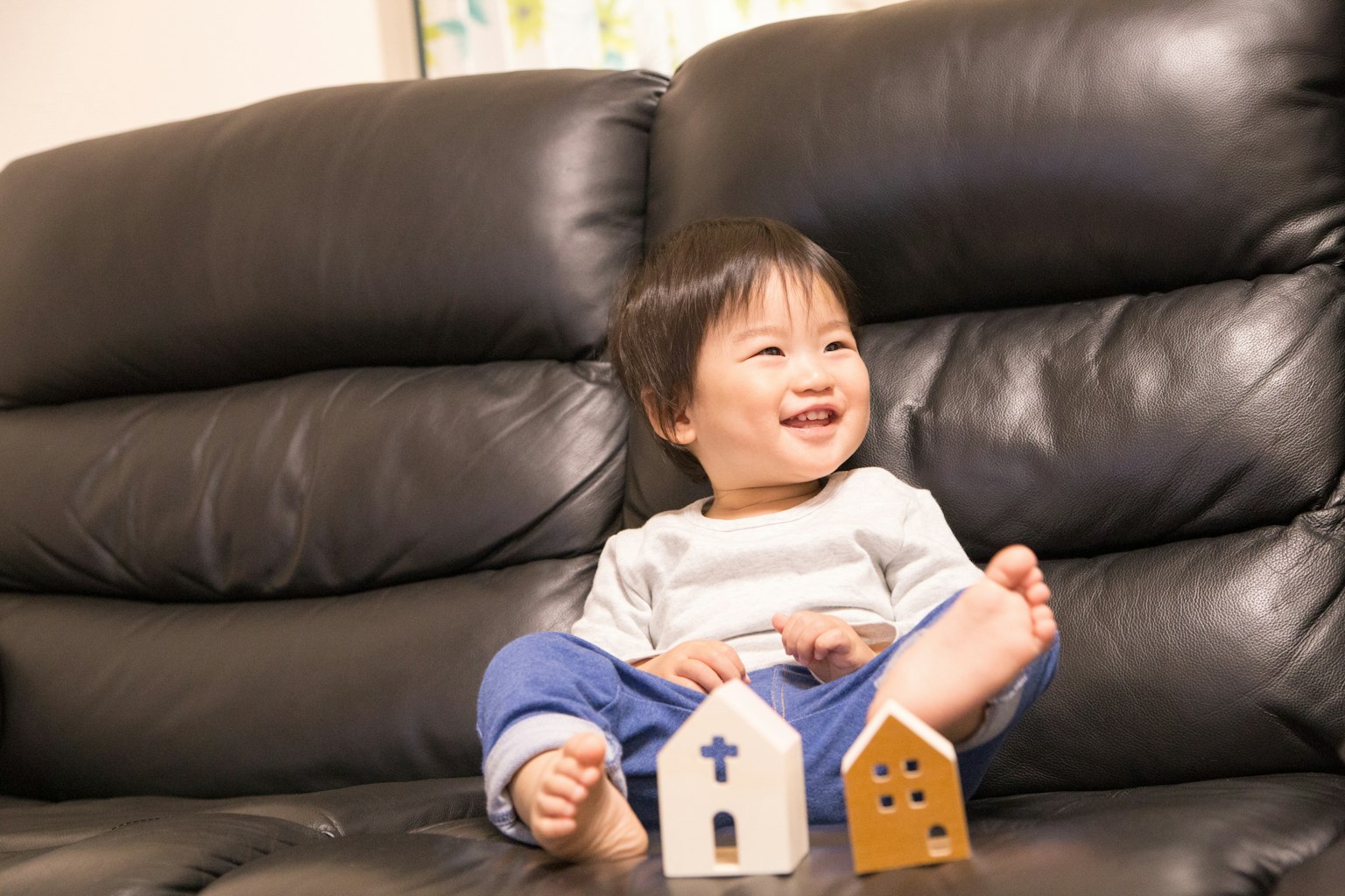 A toddler sitting on a sofa smiling with wooden house toys