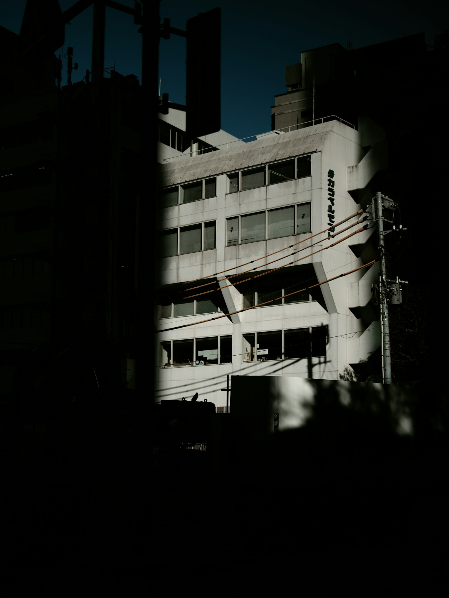Modern building partially illuminated against a dark background with power lines
