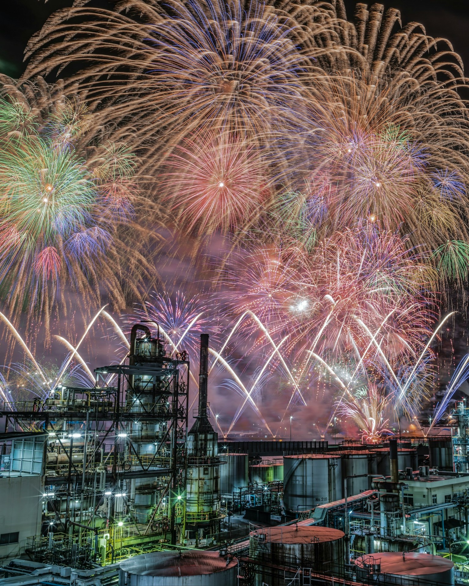 Des feux d'artifice colorés illuminent un paysage industriel la nuit