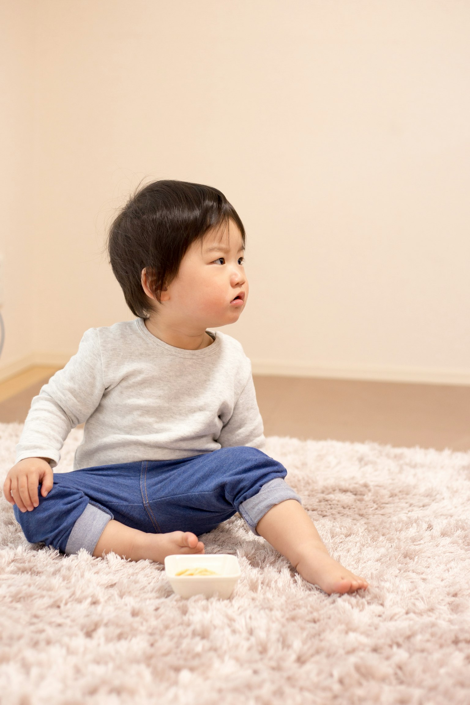 Trẻ nhỏ ngồi trên thảm màu sáng mềm mại nhìn sang một bên
