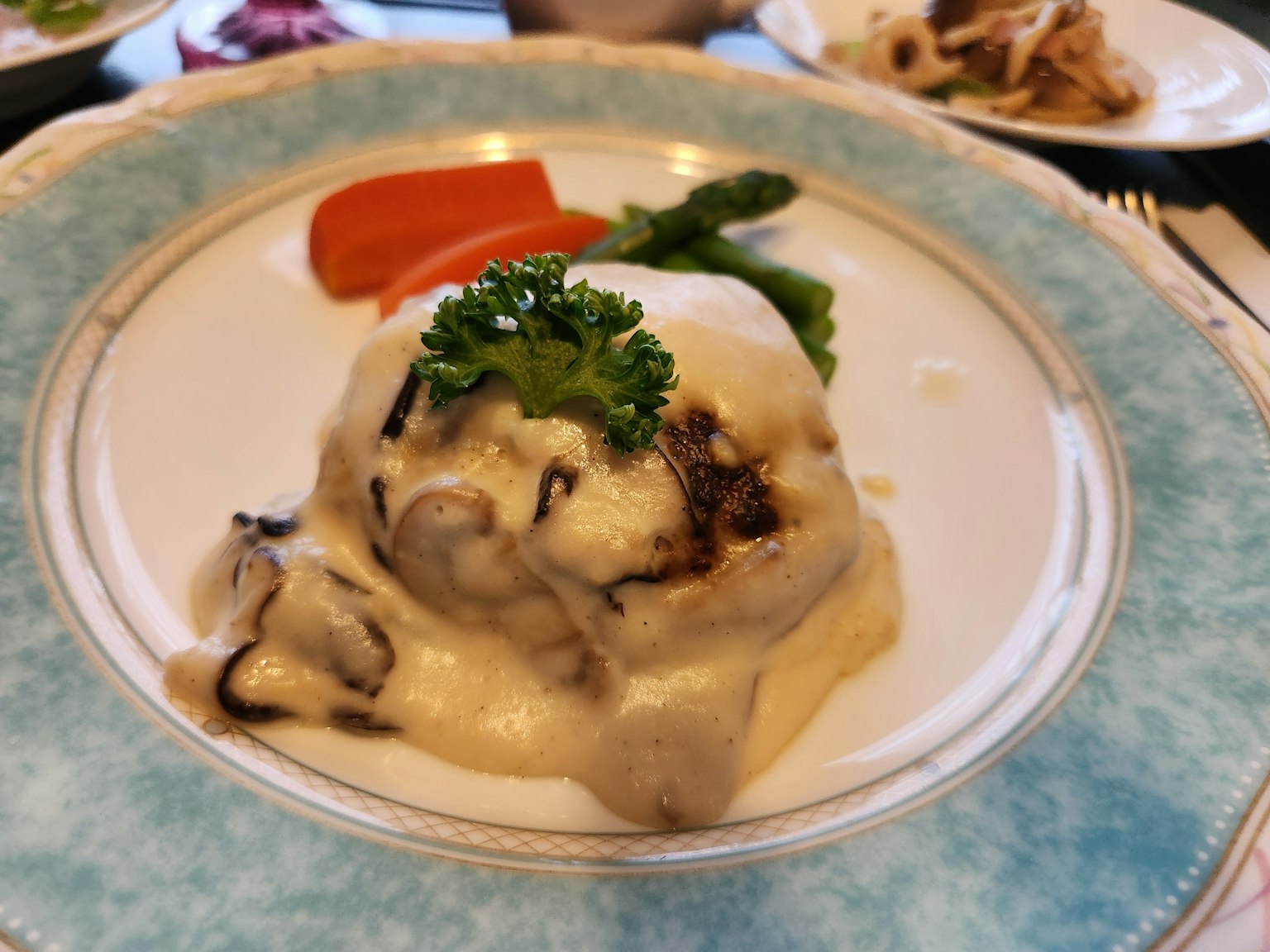 Plate of meat dish topped with creamy sauce garnished with parsley and served with vegetables