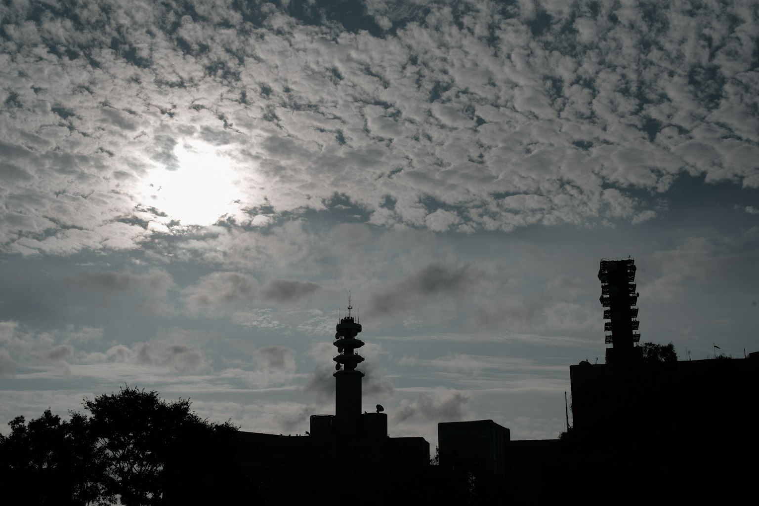 Silhouetted buildings against a cloudy sky with the sun peeking through