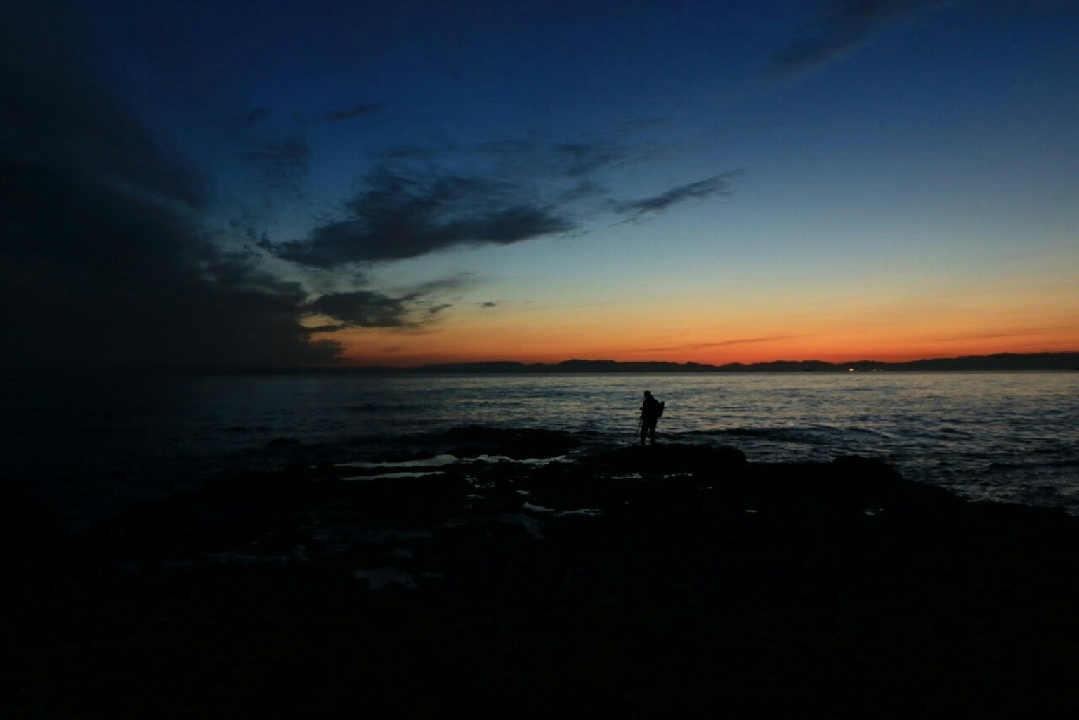 Silhouette einer Person, die am Meer bei Sonnenuntergang angelt