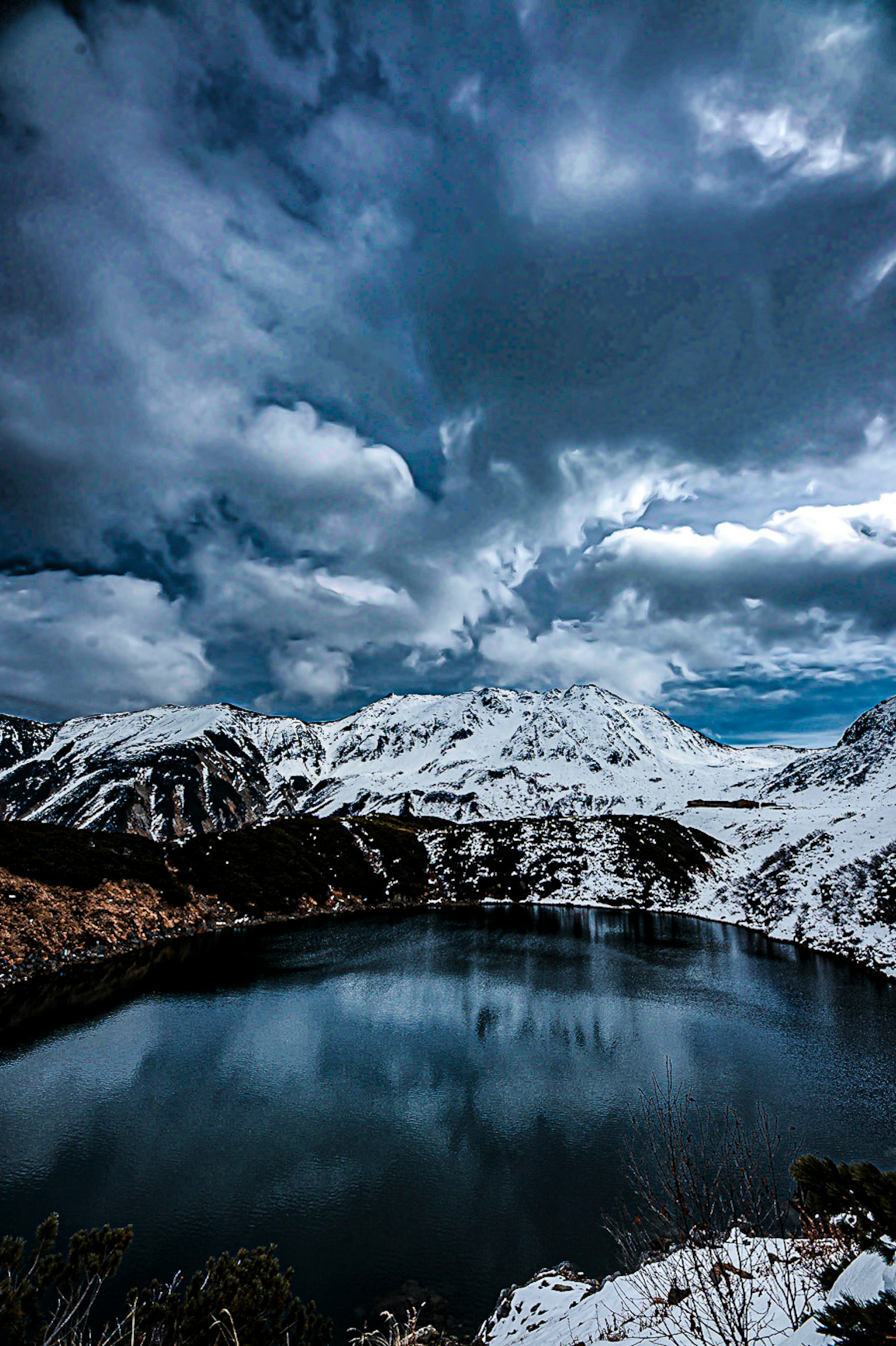 A tranquil lake reflecting snow-covered mountains and dark clouds