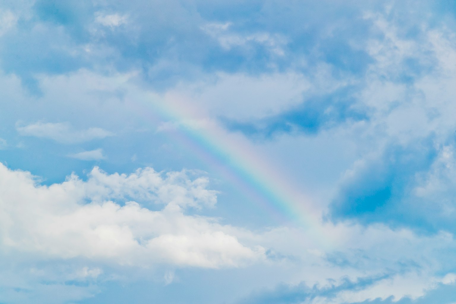 Blasser Regenbogen über einem blauen Himmel mit weißen Wolken