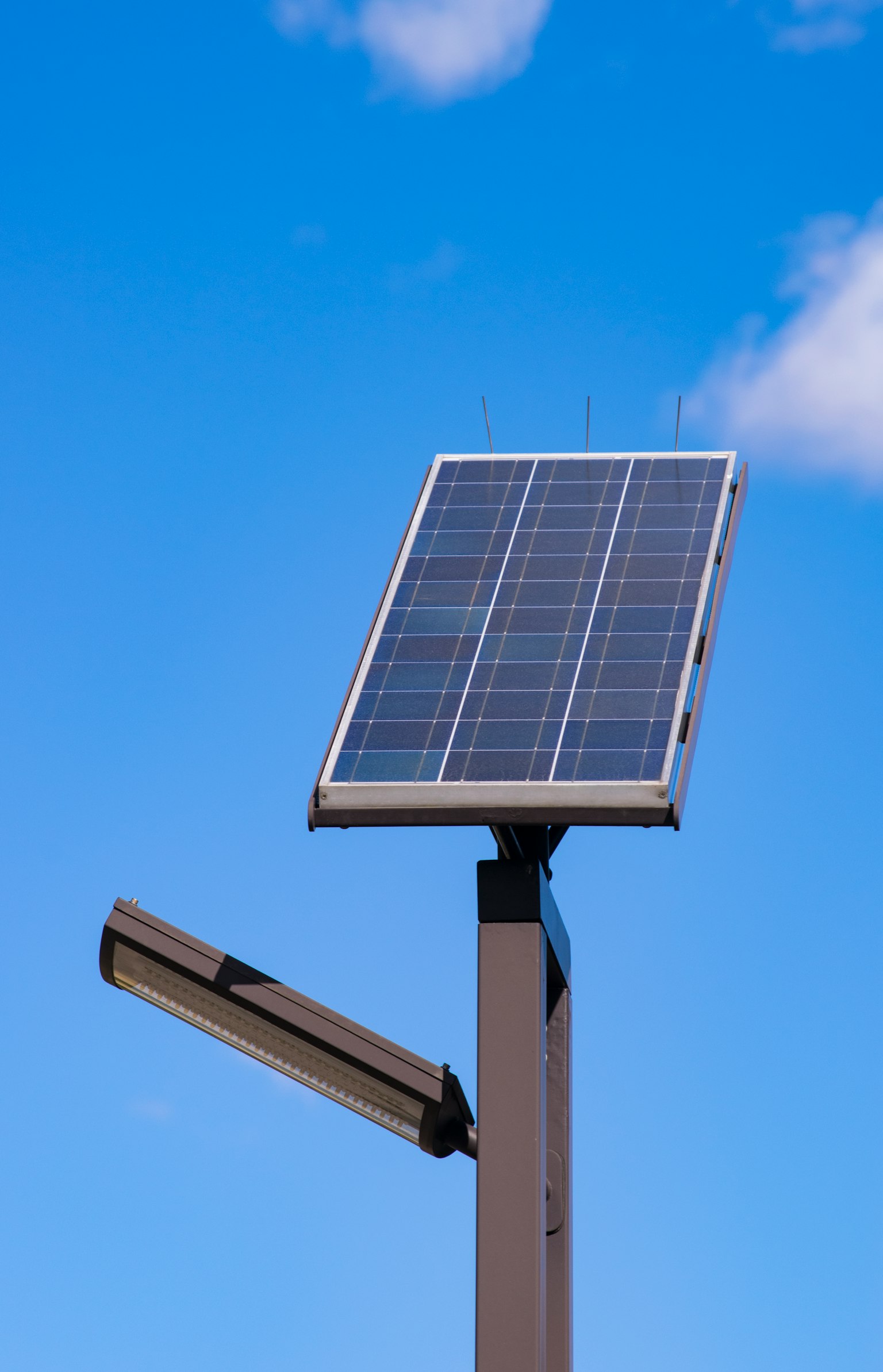 Pannello solare montato su un palo con un lampione sotto un cielo blu