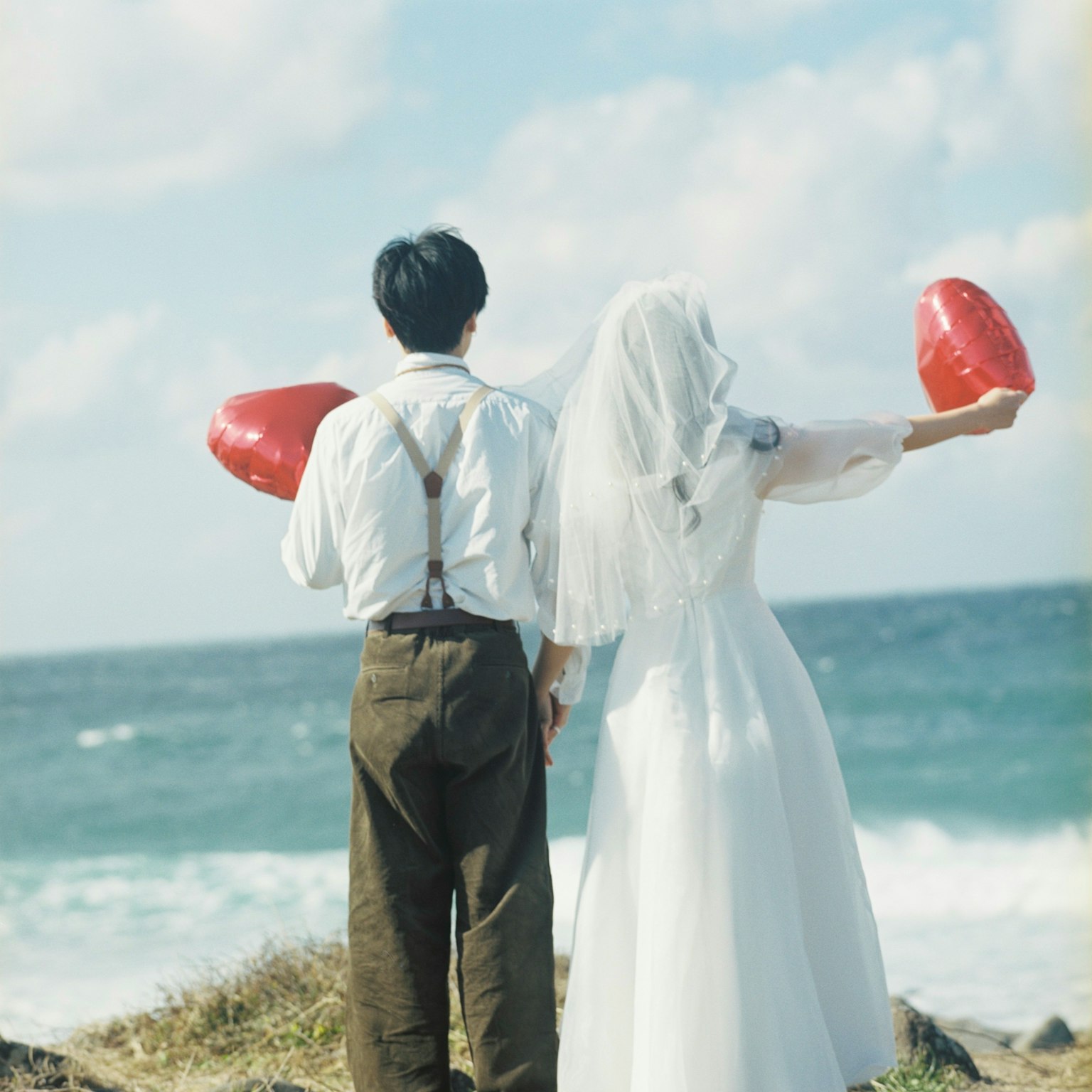 Paar mit roten Herzluftballons am Meer