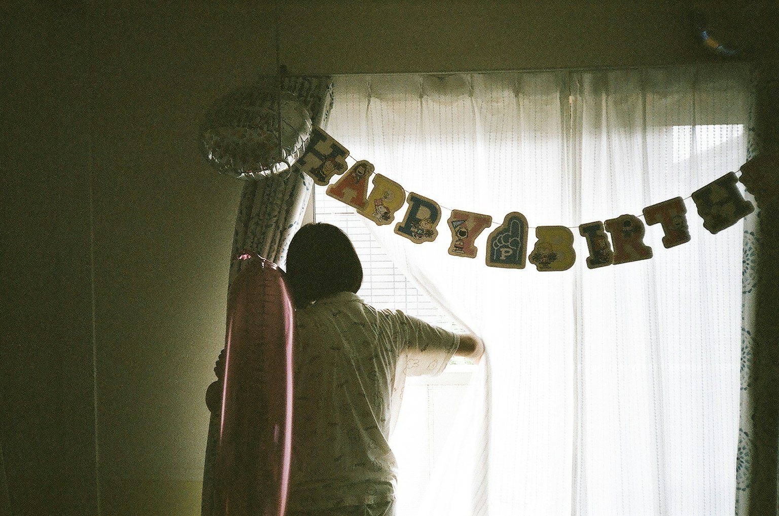 Una persona che apre le tende con un banner di compleanno in un ambiente interno accogliente