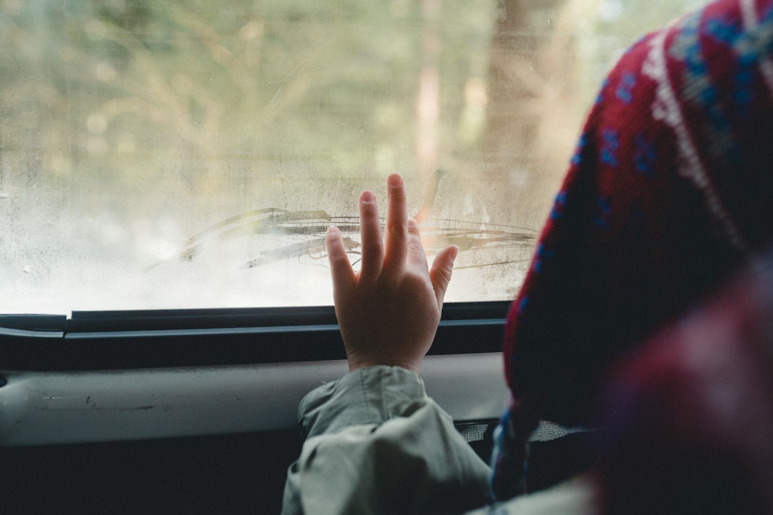 Tangan anak di jendela mobil berkabut dengan sweater berwarna-warni