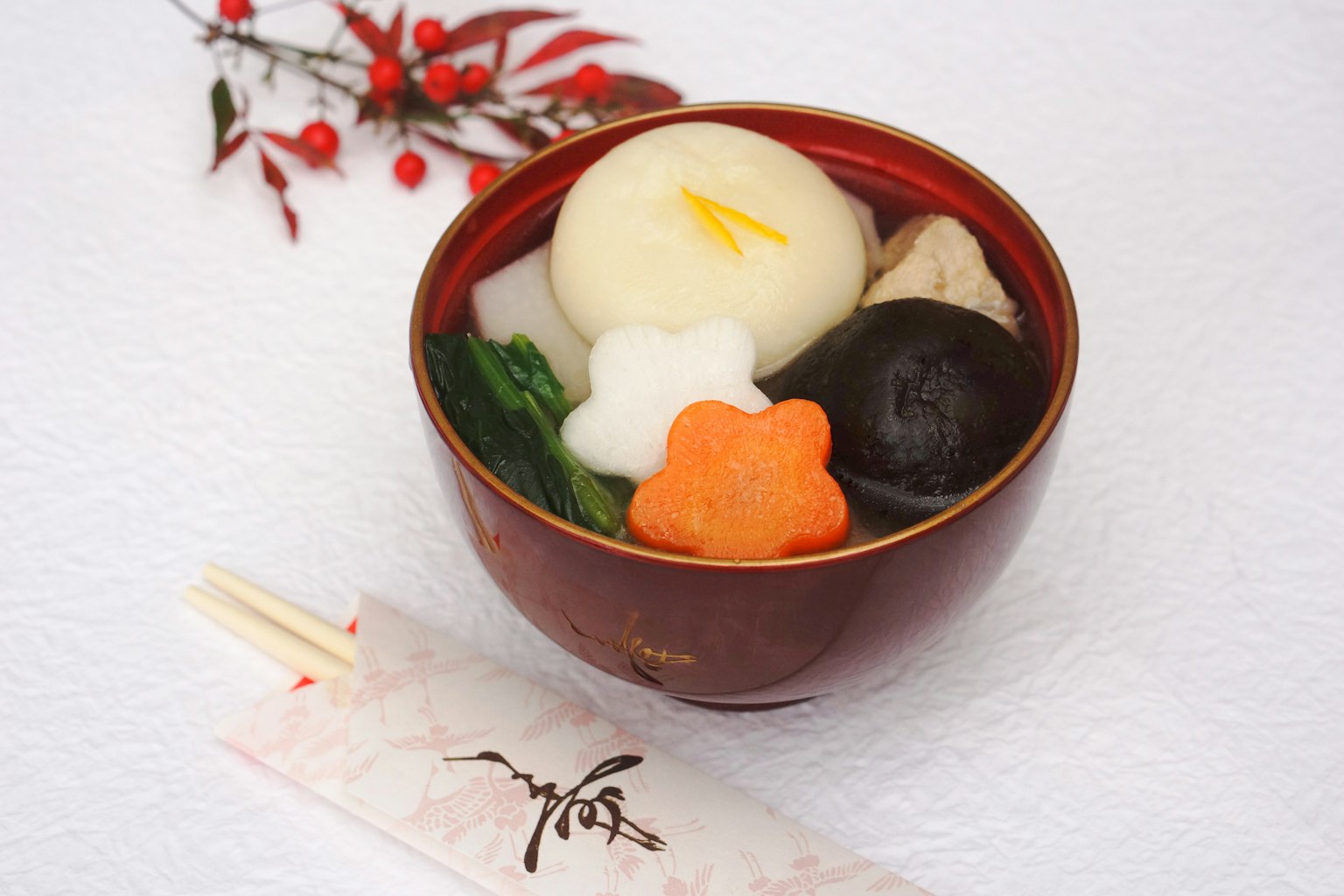 Un plato japonés tradicional servido en un tazón rojo con ingredientes coloridos que incluyen mochi blanco champiñones negros y verduras naranjas y verdes
