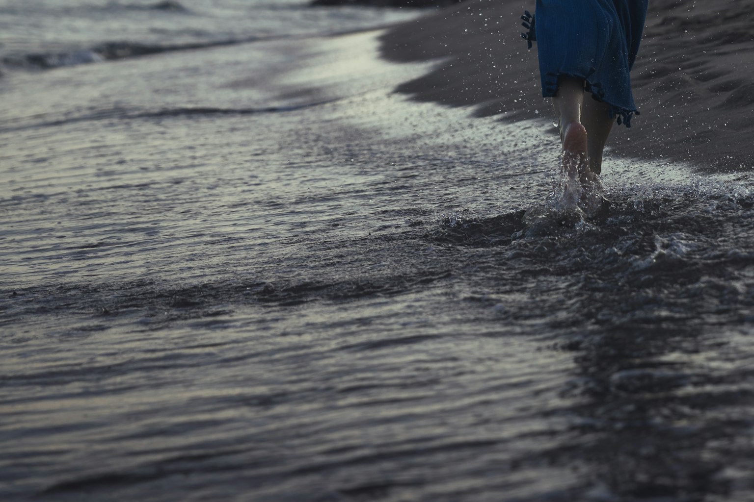 Eine Person geht am Ufer entlang mit einer Silhouette in blauer Kleidung, die sich auf der Wasseroberfläche spiegelt