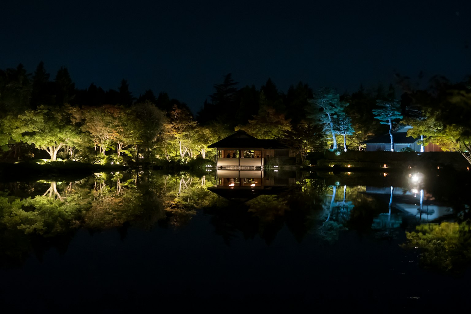 寧靜的夜景，池塘上照亮的樹木和涼亭在水中倒影