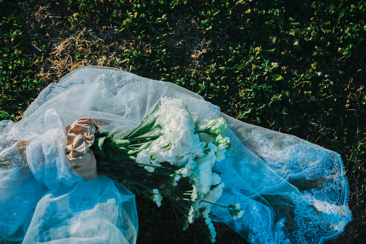 Hand holding a bouquet of white flowers wrapped in blue fabric on grass