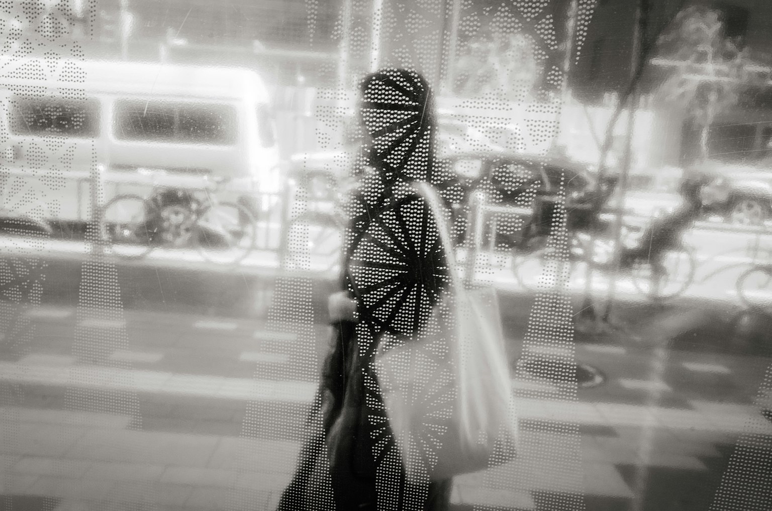 Une personne marchant dans une scène urbaine en noir et blanc avec des motifs complexes réfléchis à travers du verre