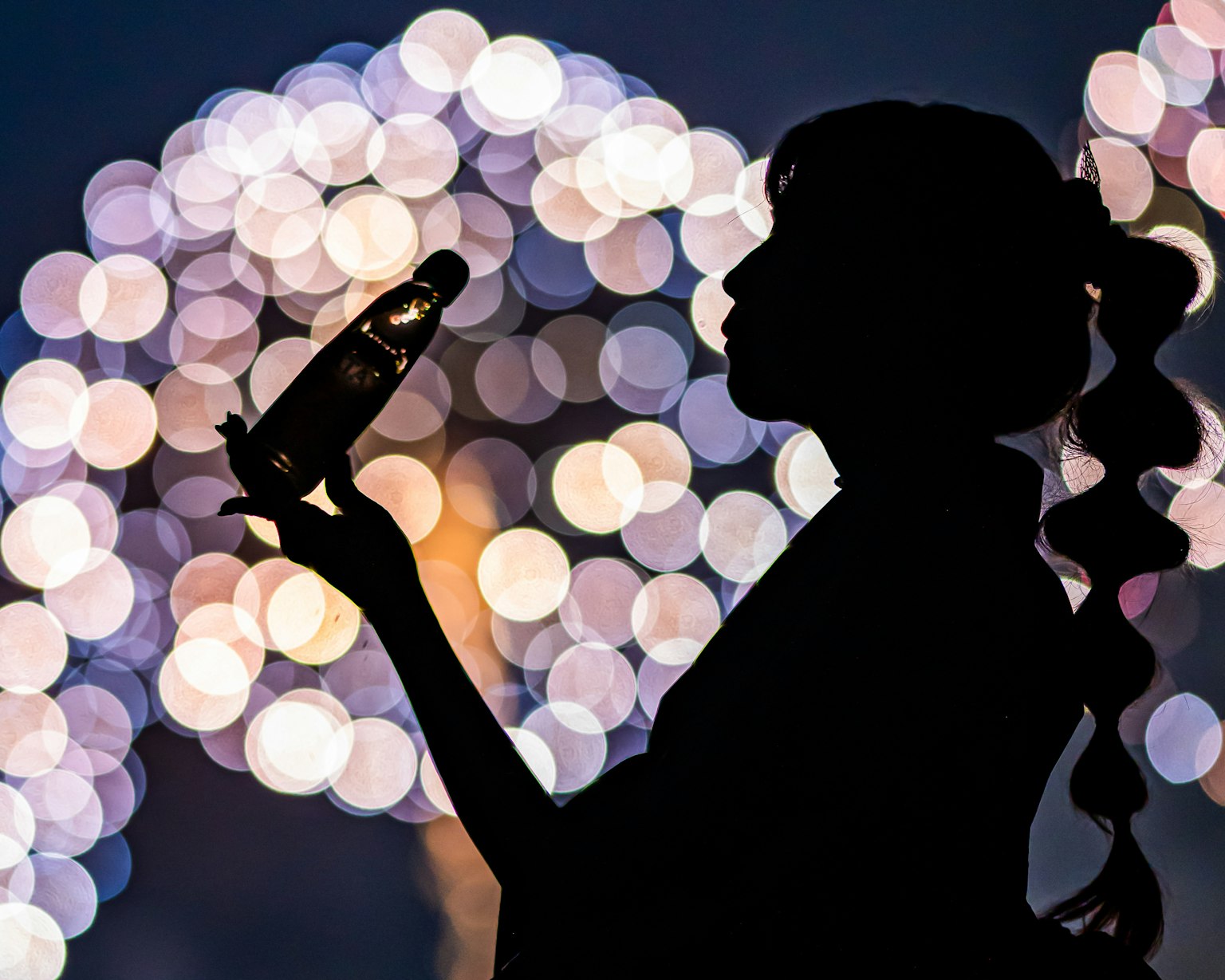 Silhouette di una donna che tiene una bottiglia di Coca-Cola con luci circolari sfocate sullo sfondo