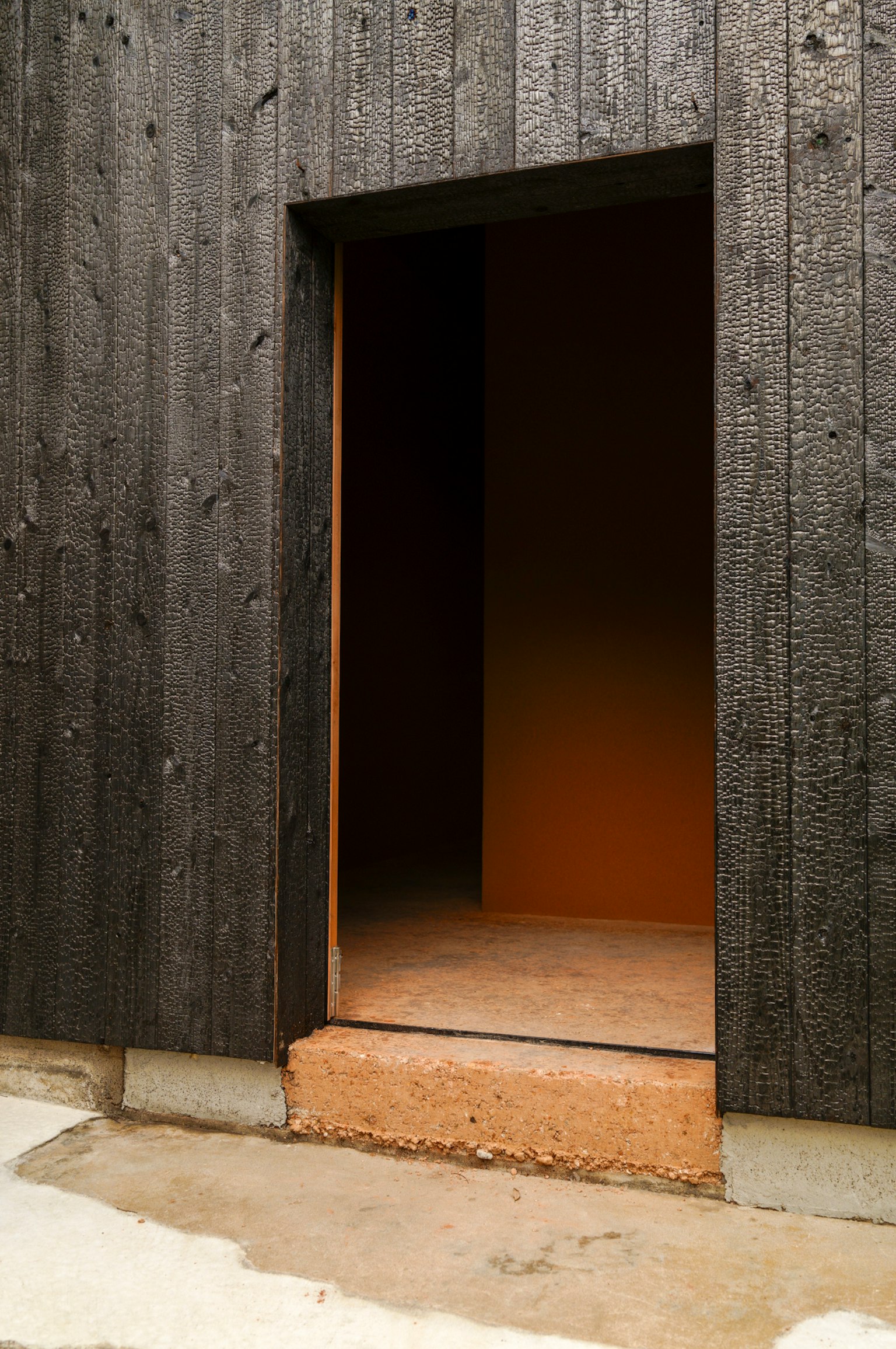 Porta aperta in un muro di legno nero con luce arancione che illumina l'interno